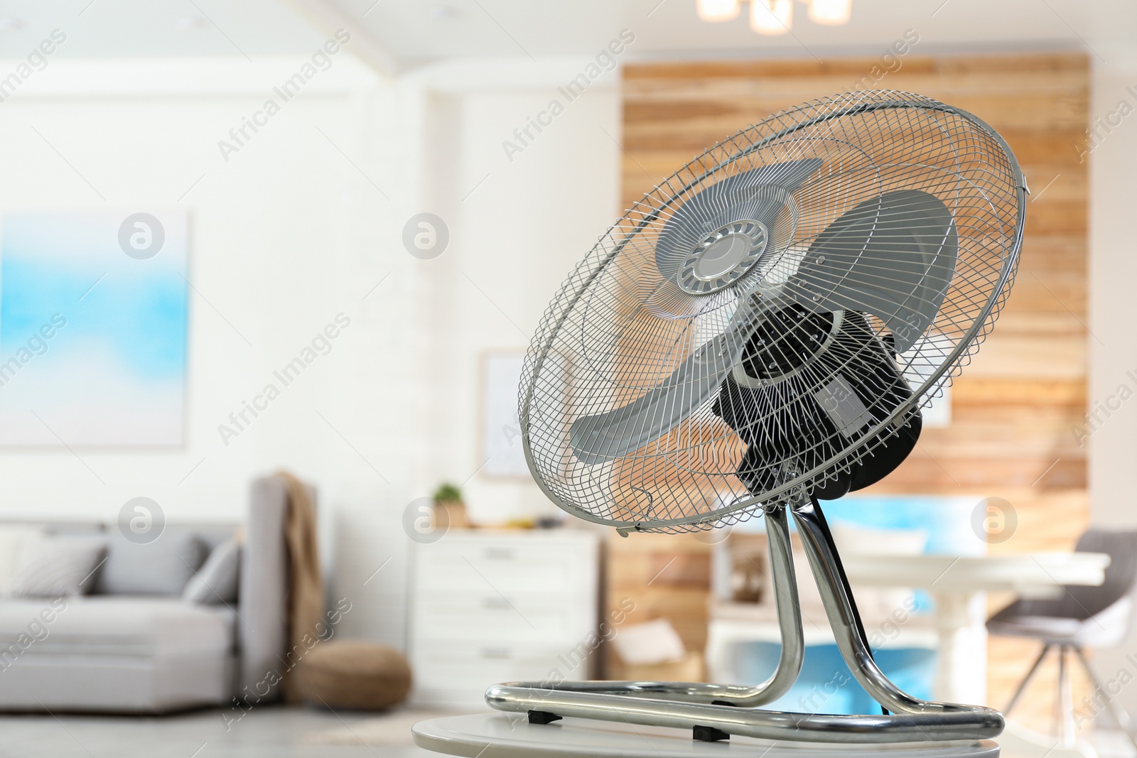 Photo of Modern electric fan on white table in living room. Space for text