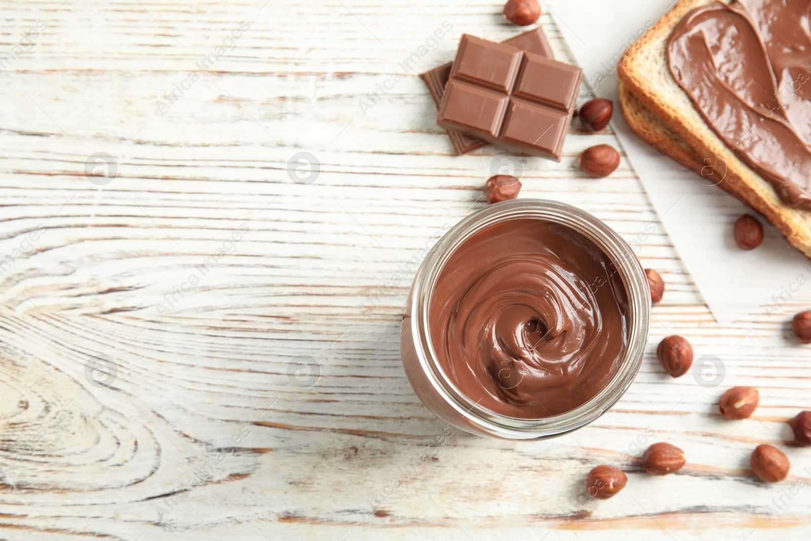 Photo of Flat lay composition with glass jar of tasty chocolate cream and hazelnuts on wooden background. Space for text