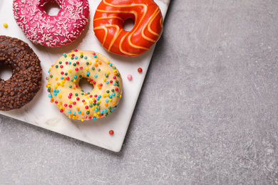 Yummy donuts with sprinkles on light grey table, top view. Space for text