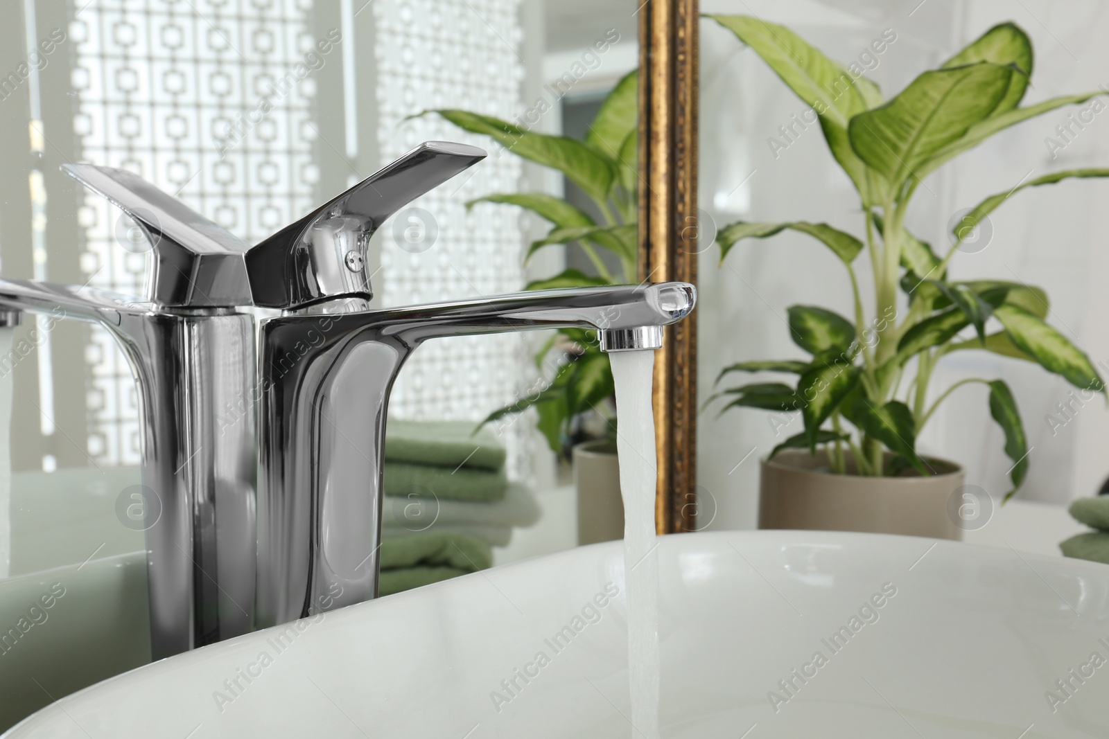 Photo of Water running from faucet into sink near mirror in bathroom, closeup