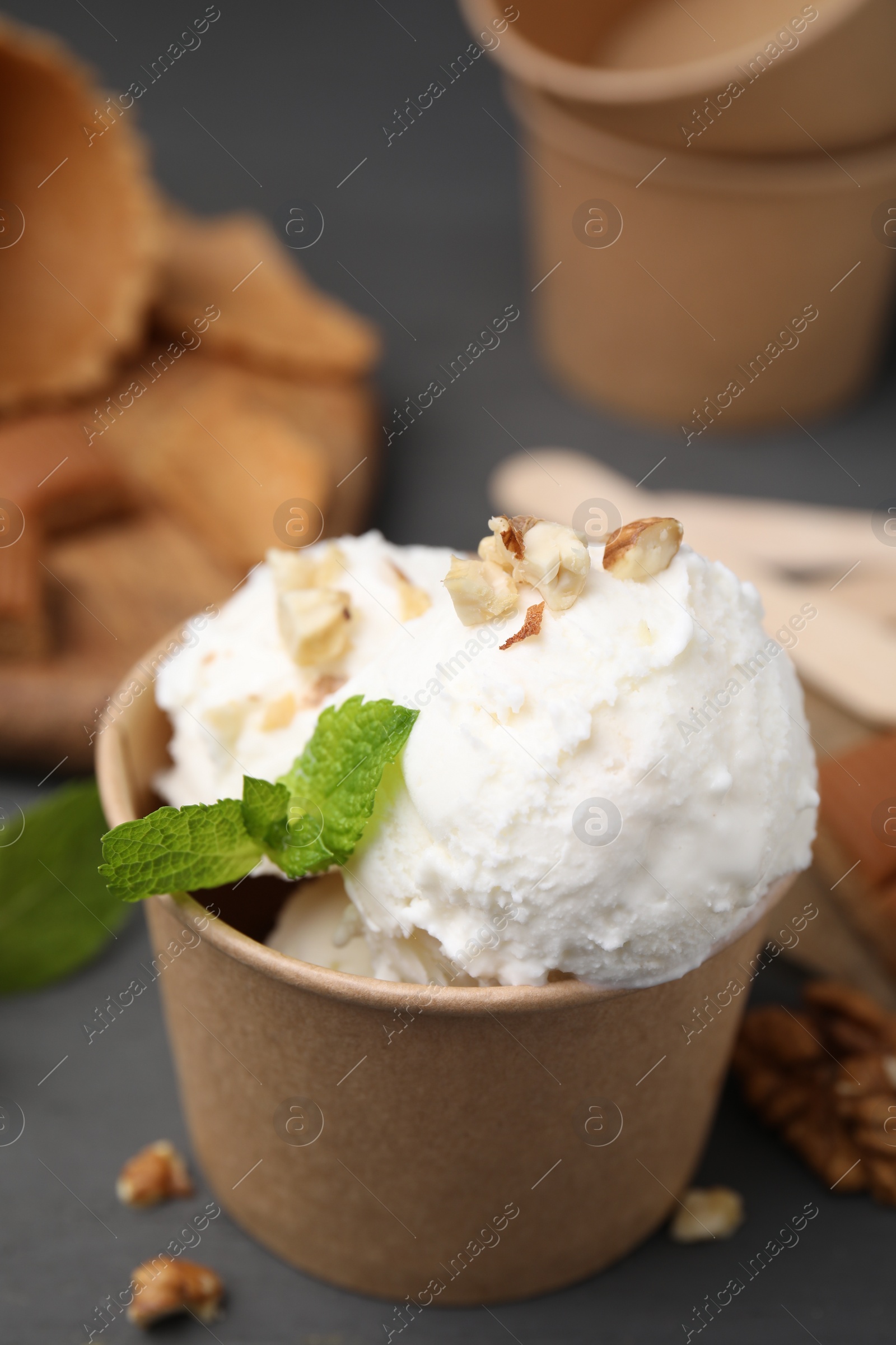 Photo of Tasty ice cream with mint and nuts in paper cup on grey table, closeup