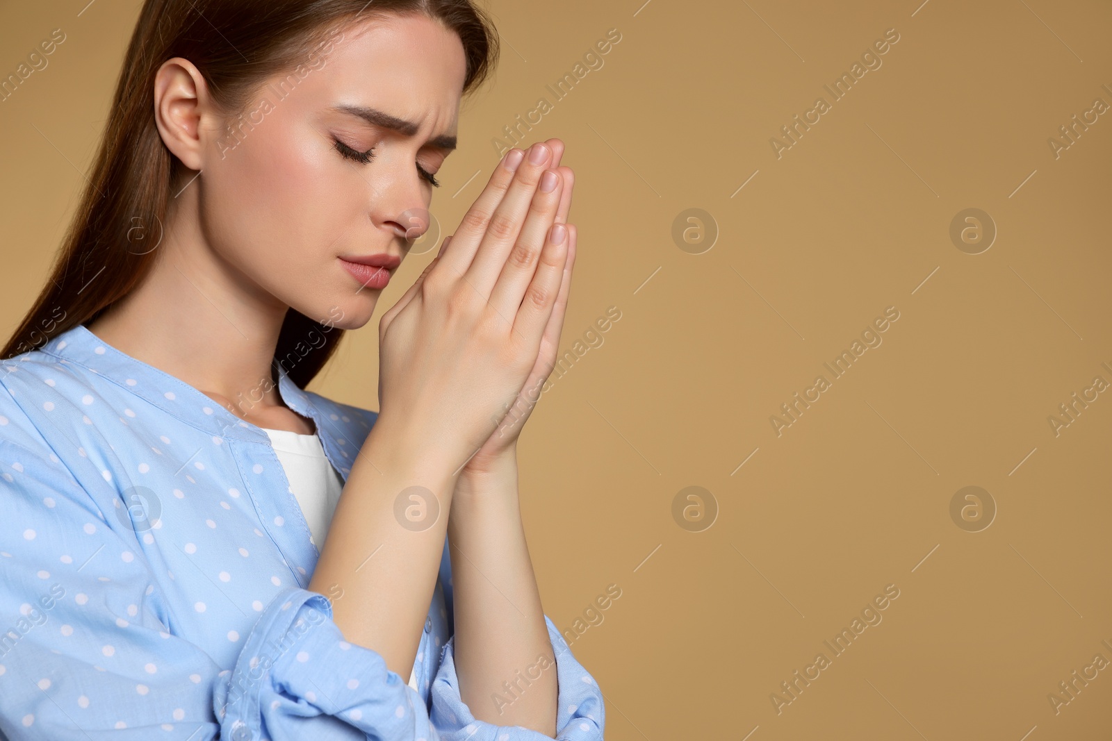 Photo of Woman with clasped hands praying on beige background, space for text