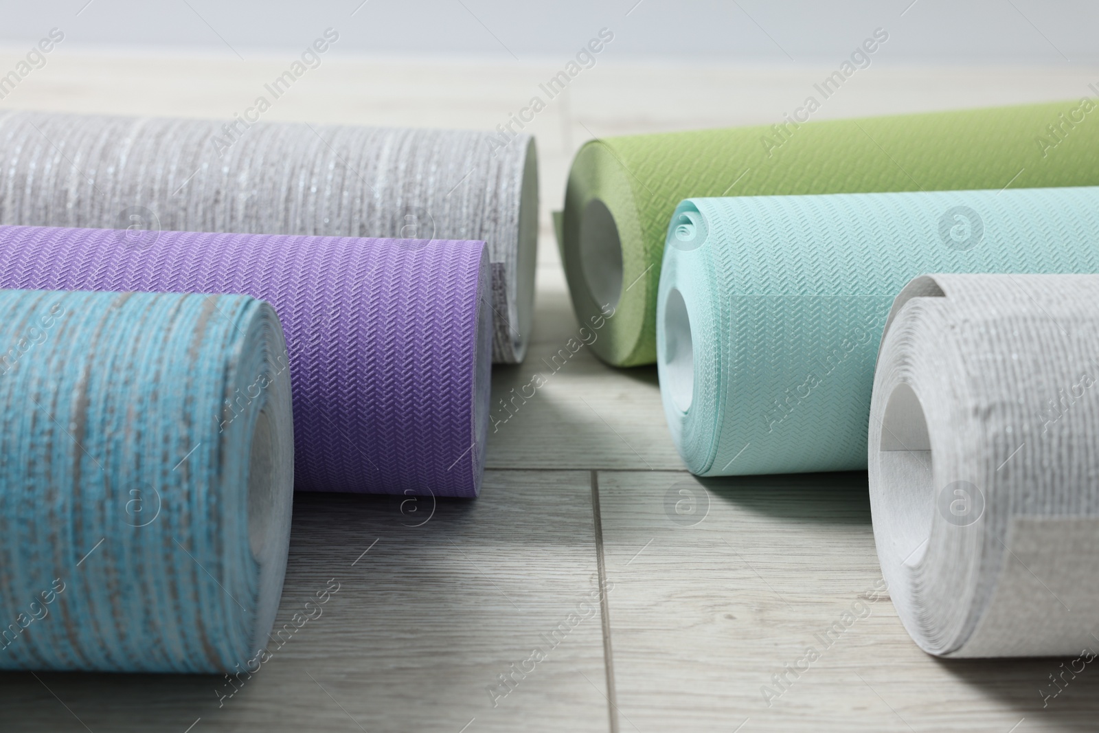 Photo of Many different wallpaper rolls on light wooden floor, closeup