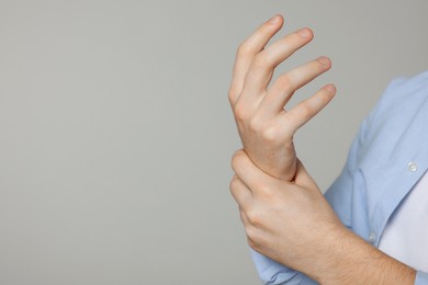 Man suffering from pain in his hand on light grey background, closeup with space for text. Arthritis symptoms