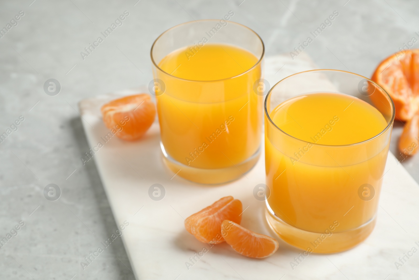 Photo of Glasses of fresh tangerine juice and fruits on light table