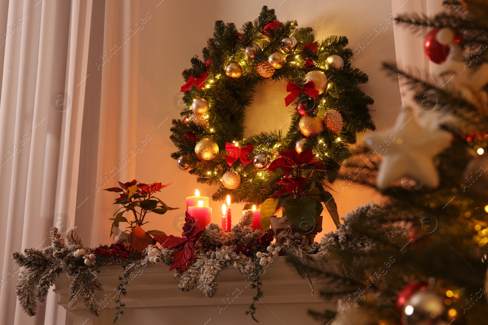 Photo of Beautiful Christmas wreath on white wall over decorated mantelshelf indoors