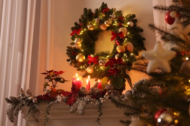 Beautiful Christmas wreath on white wall over decorated mantelshelf indoors