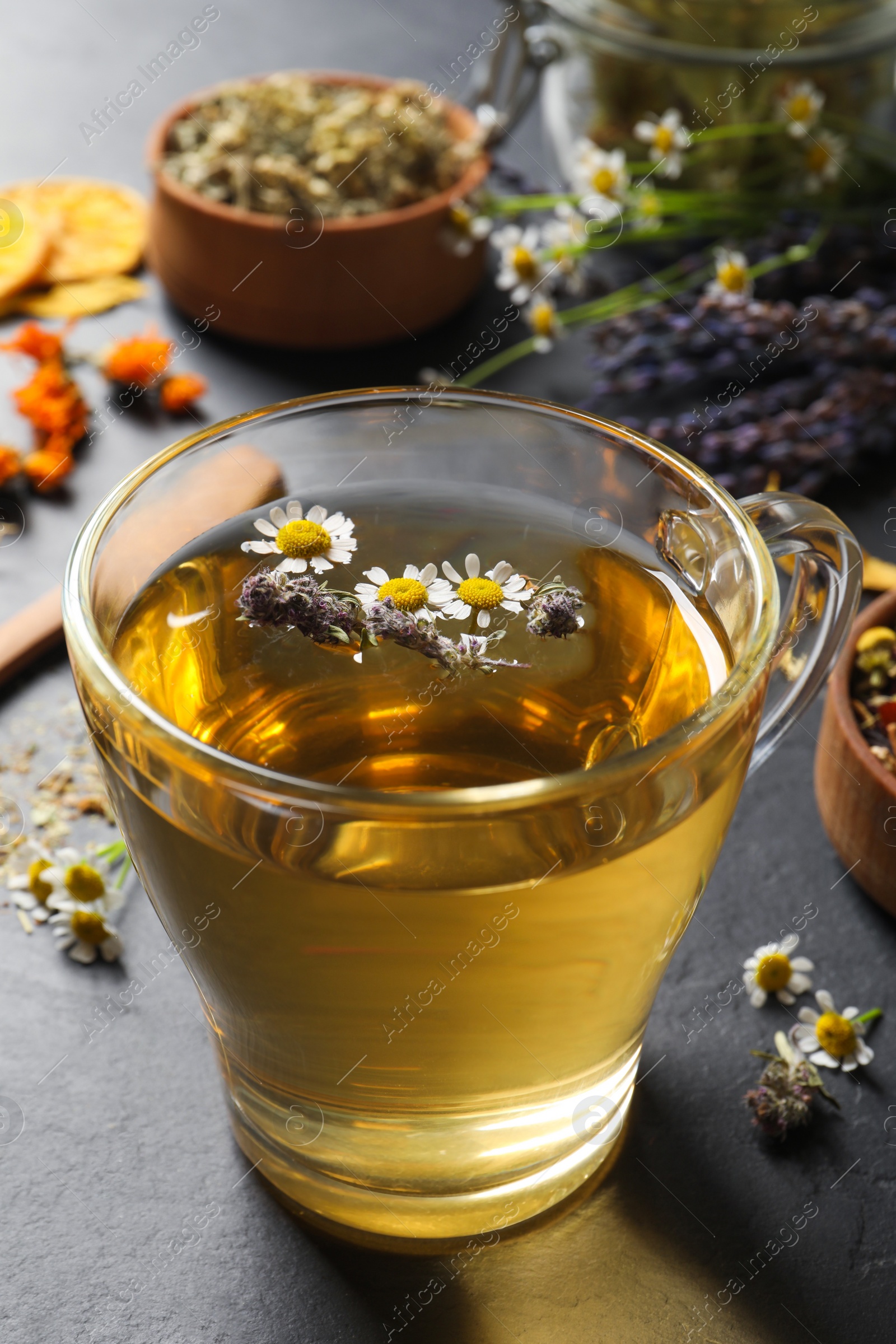 Photo of Glass cup of aromatic freshly brewed tea near different dry herbs on black table