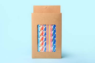 Box with many paper drinking straws on light blue background