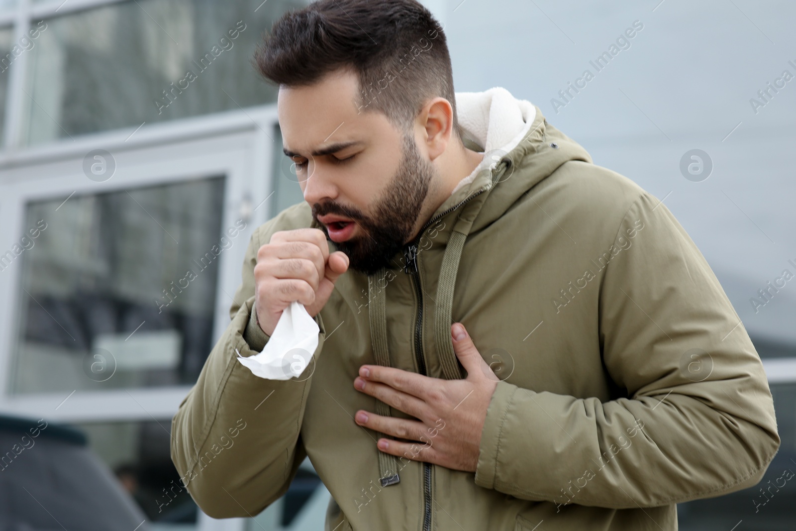 Photo of Sick man with tissue coughing outdoors. Cold symptoms