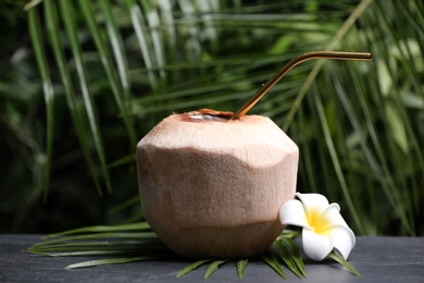 Photo of Young peeled coconut with straw and flower on black table