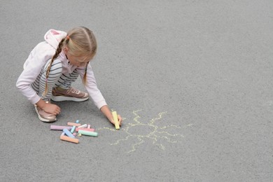 Photo of Little child drawing sun with chalk on asphalt, space for text