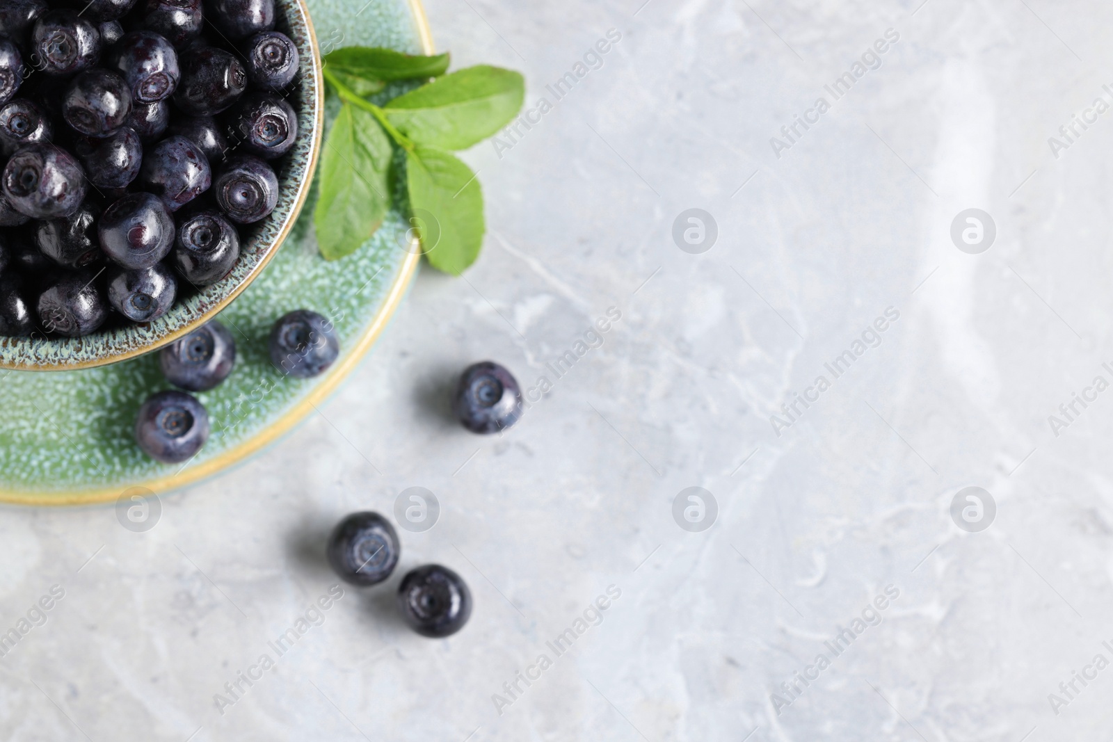 Photo of Tasty fresh bilberries in bowl on white table, flat lay. Space for text