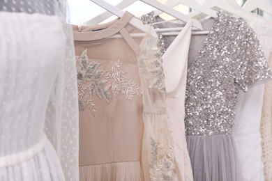 Photo of Hangers with different beautiful dresses in atelier, closeup