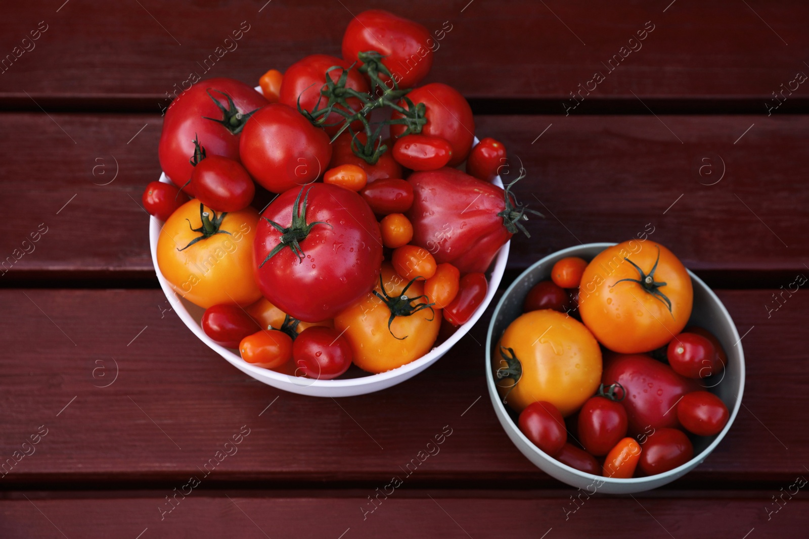 Photo of Bowls with fresh tomatoes on wooden table, above view