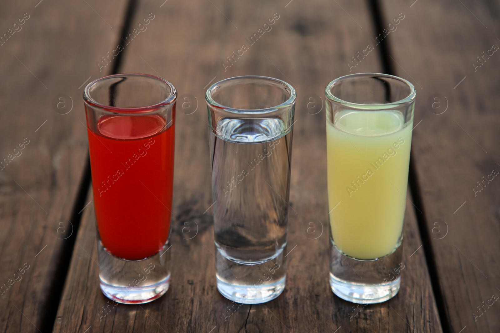 Photo of Shots with lime juice, tequila and sangria as colors of mexican flag on wooden table, closeup. Traditional serving