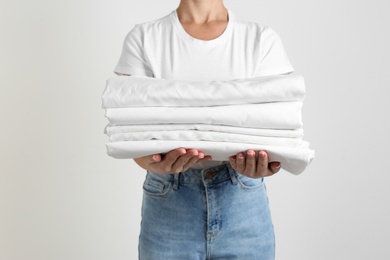 Photo of Woman holding stack of clean bed linens on light grey background