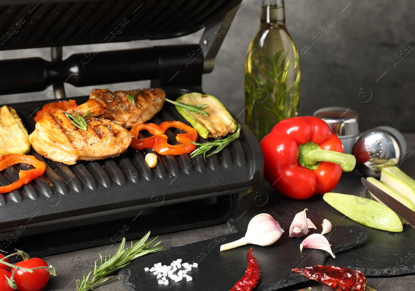 Photo of Electric grill with different products on grey textured table