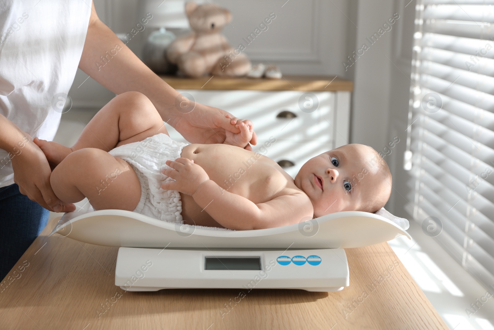 Photo of Young woman weighting her cute baby at home, closeup. Health care