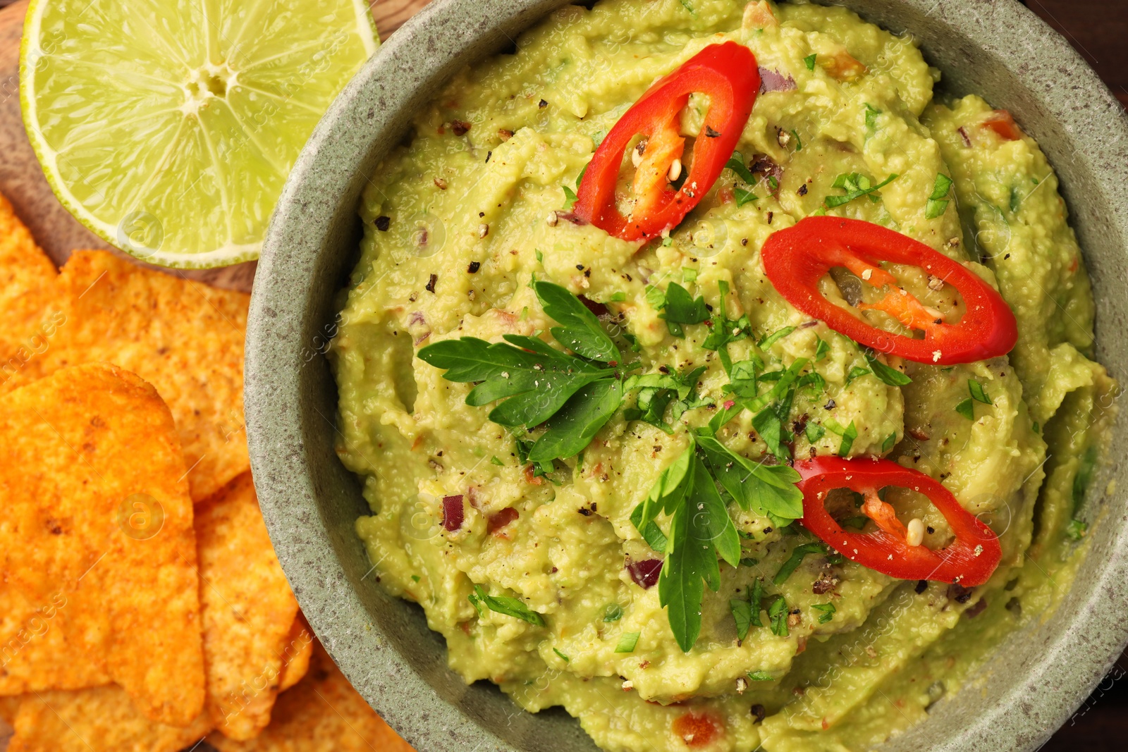 Photo of Bowl of delicious guacamole, lime and nachos chips on table, flat lay