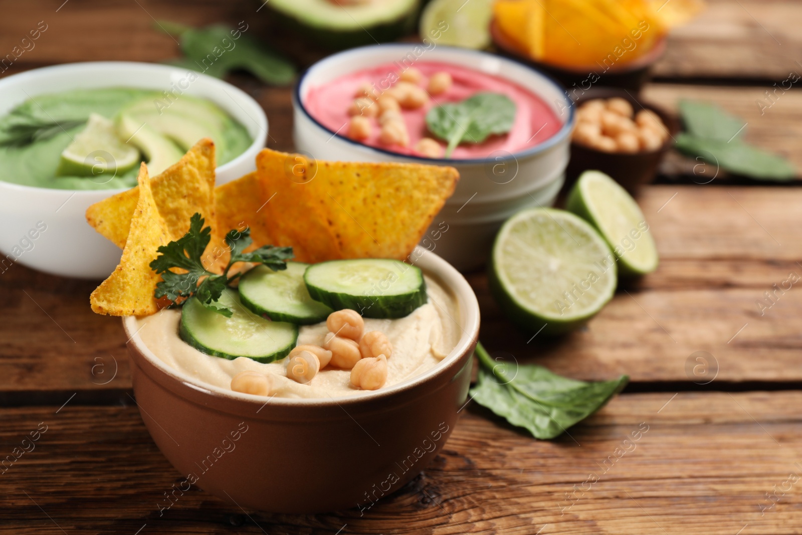 Photo of Bowl of delicious classic hummus with tortilla chips, cucumber and parsley on wooden table. Space for text
