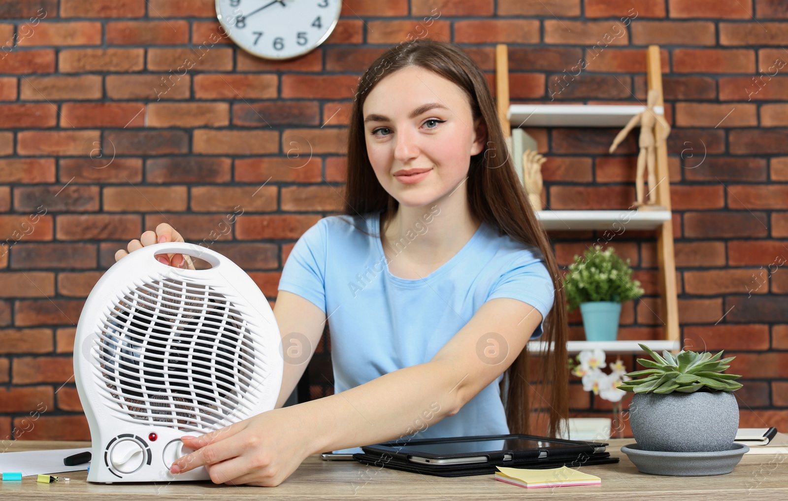 Photo of Woman adjusting temperature on electric infrared heater at wooden table indoors