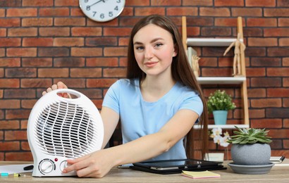 Photo of Woman adjusting temperature on electric infrared heater at wooden table indoors