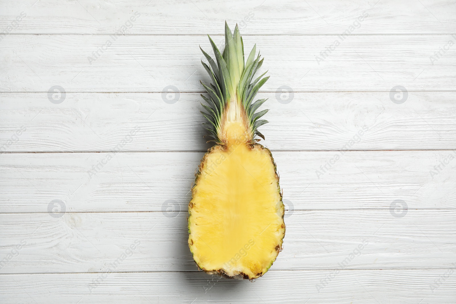 Photo of Half of fresh pineapple on white wooden background, top view