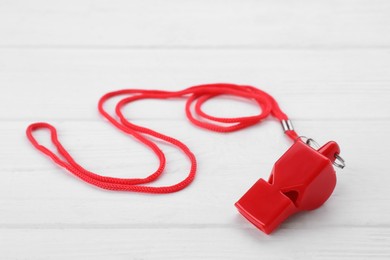 One red whistle with cord on white wooden table