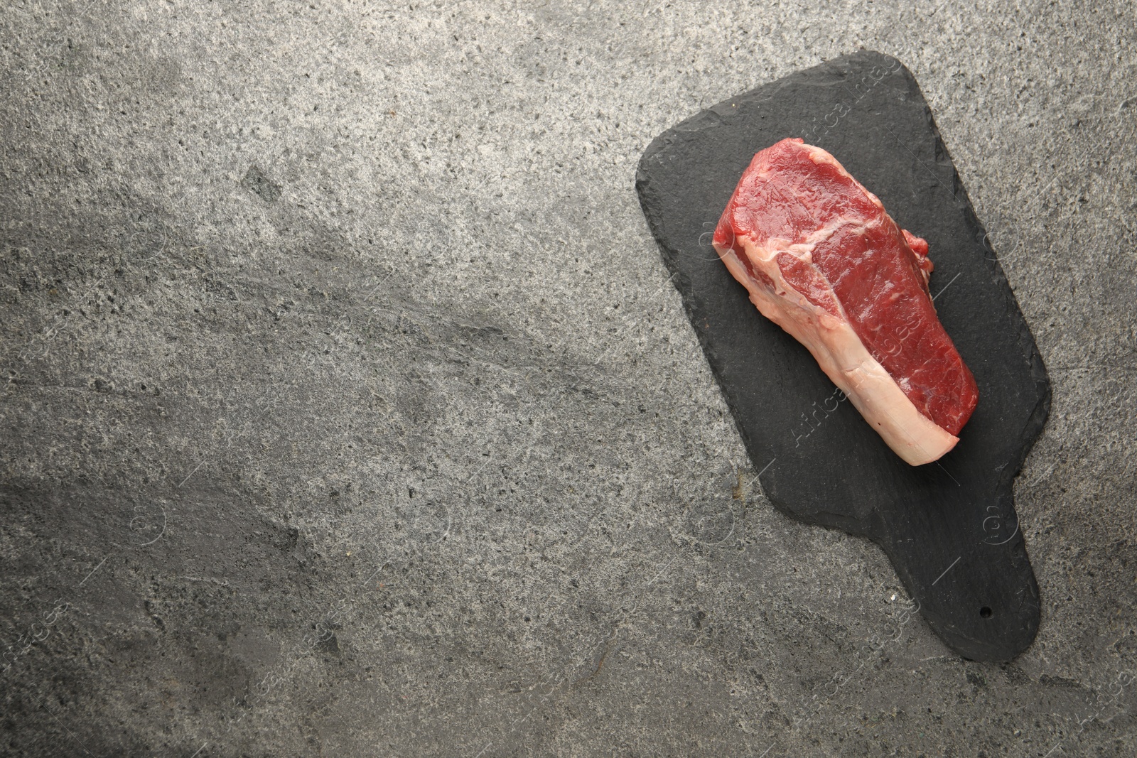 Photo of Piece of raw beef meat on grey textured table, top view. Space for text
