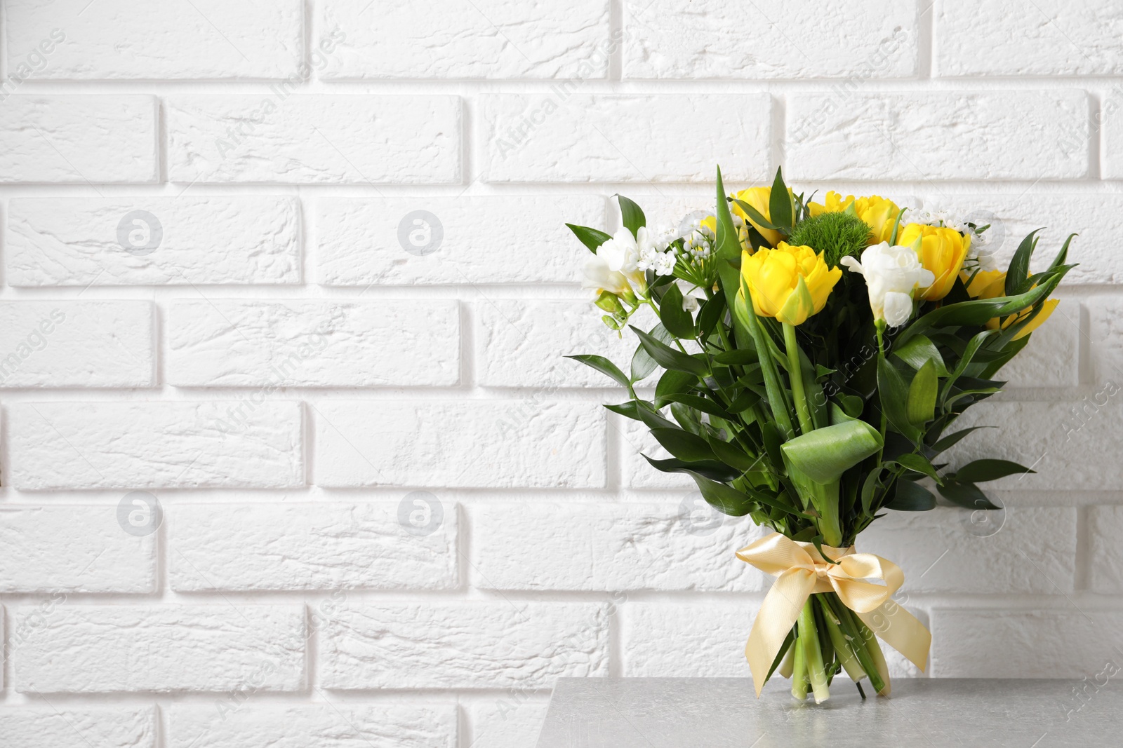 Photo of Beautiful bouquet with peony tulips on light table near white brick wall. Space for text