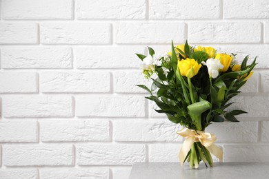 Photo of Beautiful bouquet with peony tulips on light table near white brick wall. Space for text
