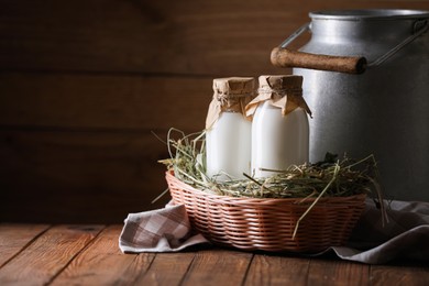 Photo of Tasty fresh milk in can and bottles on wooden table, space for text