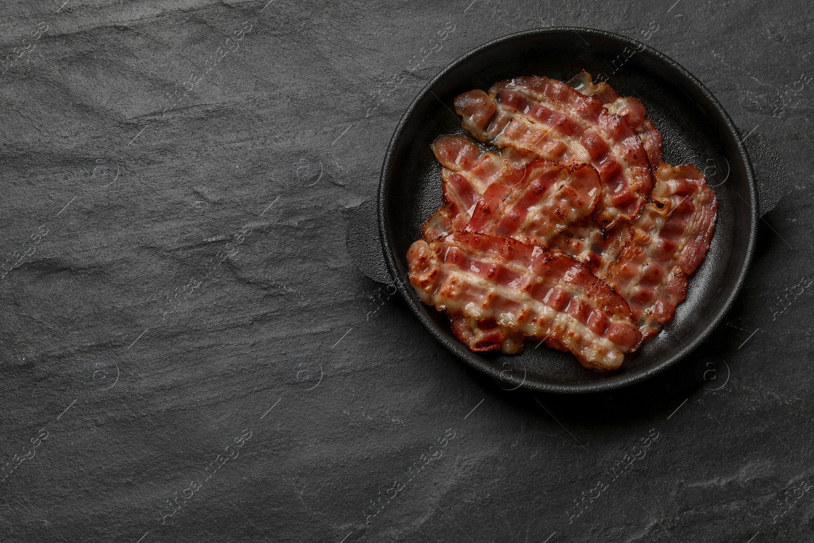 Photo of Fried bacon slices on dark textured table, top view. Space for text
