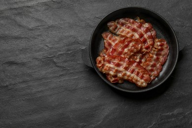 Photo of Fried bacon slices on dark textured table, top view. Space for text