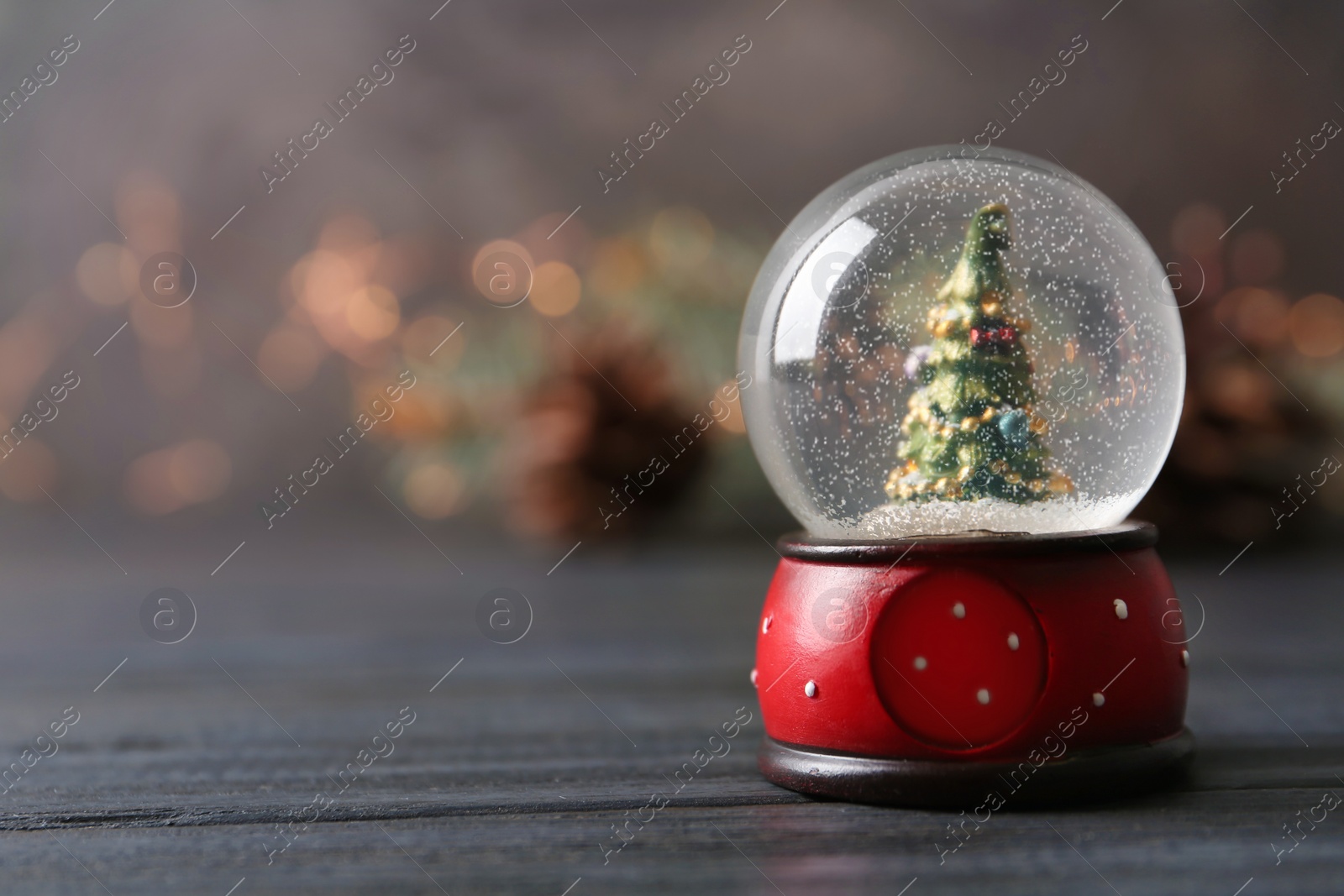 Photo of Snow globe with Christmas tree on grey wooden table against festive lights, space for text