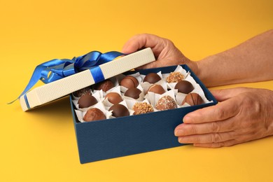Photo of Woman opening box of delicious chocolate candies on yellow background, closeup