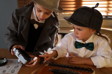 Cute little detectives with vintage camera at table in office