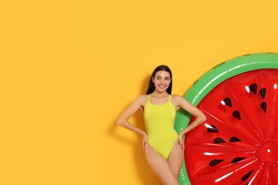 Photo of Young woman in stylish swimsuit near inflatable mattress against orange background. Space for text