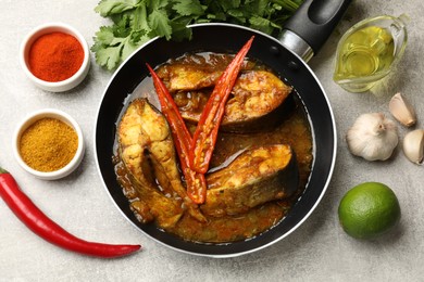 Photo of Tasty fish curry in frying pan and ingredients on light grey table, flat lay. Indian cuisine