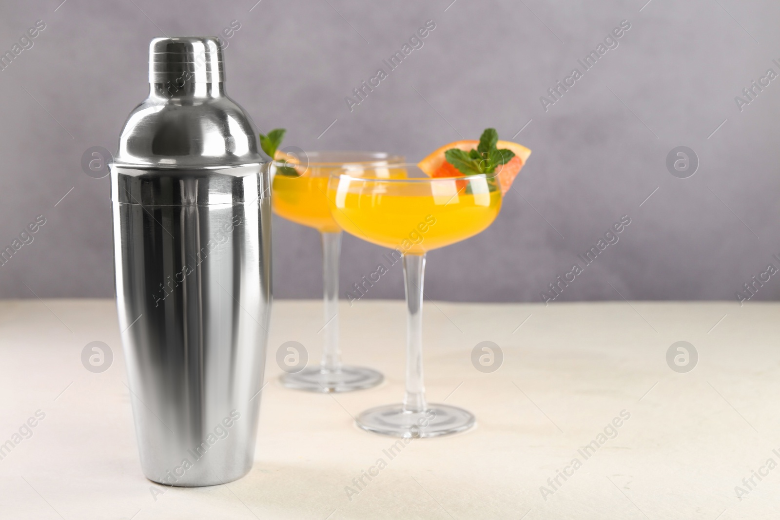 Photo of Metal shaker and delicious cocktails on light table, space for text