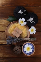 Photo of Spa composition. Sea salt, soap bar, herbal bags and flowers on wooden table, flat lay