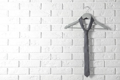 Photo of Tie on wooden hanger against brick wall. Space for text