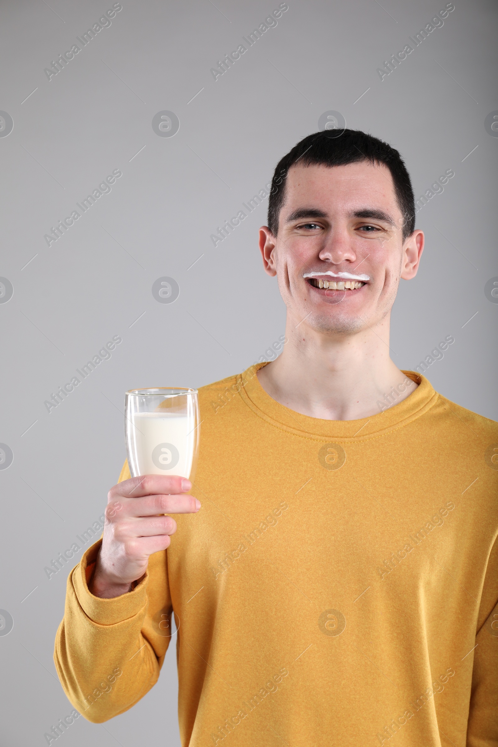 Photo of Happy man with milk mustache holding glass of tasty dairy drink on gray background