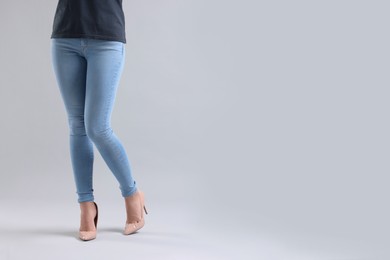 Woman wearing stylish jeans and high heels shoes on light gray background, closeup. Space for text