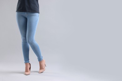 Photo of Woman wearing stylish jeans and high heels shoes on light gray background, closeup. Space for text