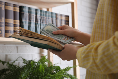 Photo of Woman hiding dollar banknotes in book indoors, closeup. Money savings