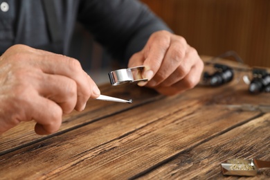 Photo of Male jeweler evaluating precious gemstone at table in workshop, closeup