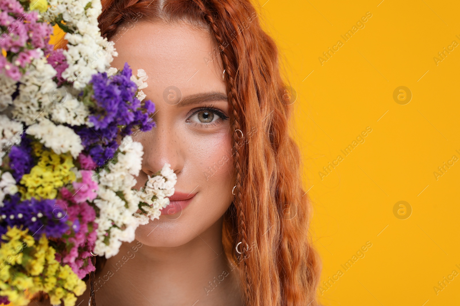 Photo of Beautiful young hippie woman and bouquet of colorful flowers on orange background, closeup. Space for text