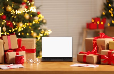 Laptop with blank screen, Christmas gifts and letters on table at home